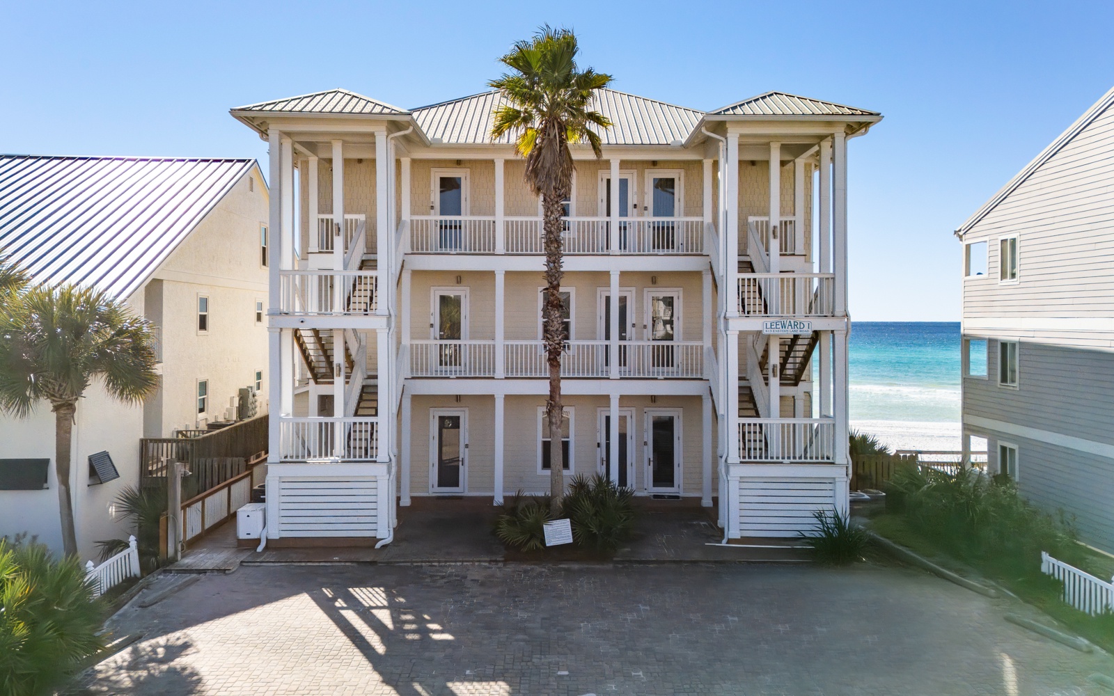 Charming beachfront building with multiple balconies overlooking turquoise waters and white sand, surrounded by swaying palms in a coastal paradise.