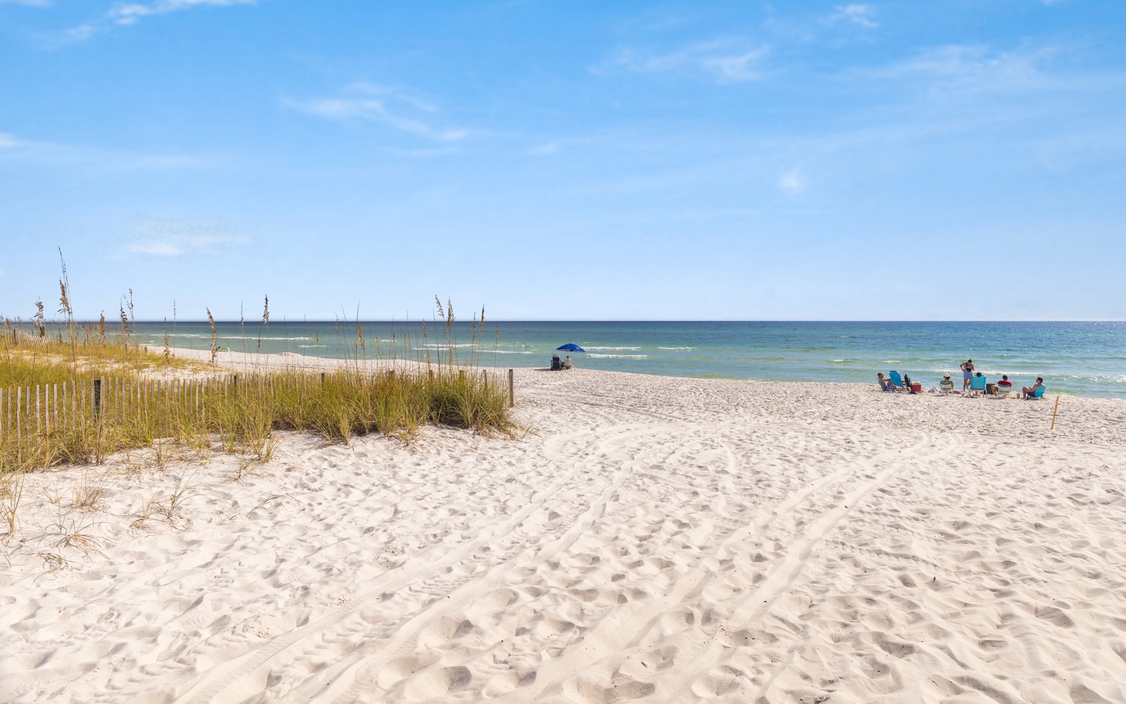 Pristine white sand beach stretches along emerald waters, with natural dunes and sea grass creating a peaceful coastal setting.