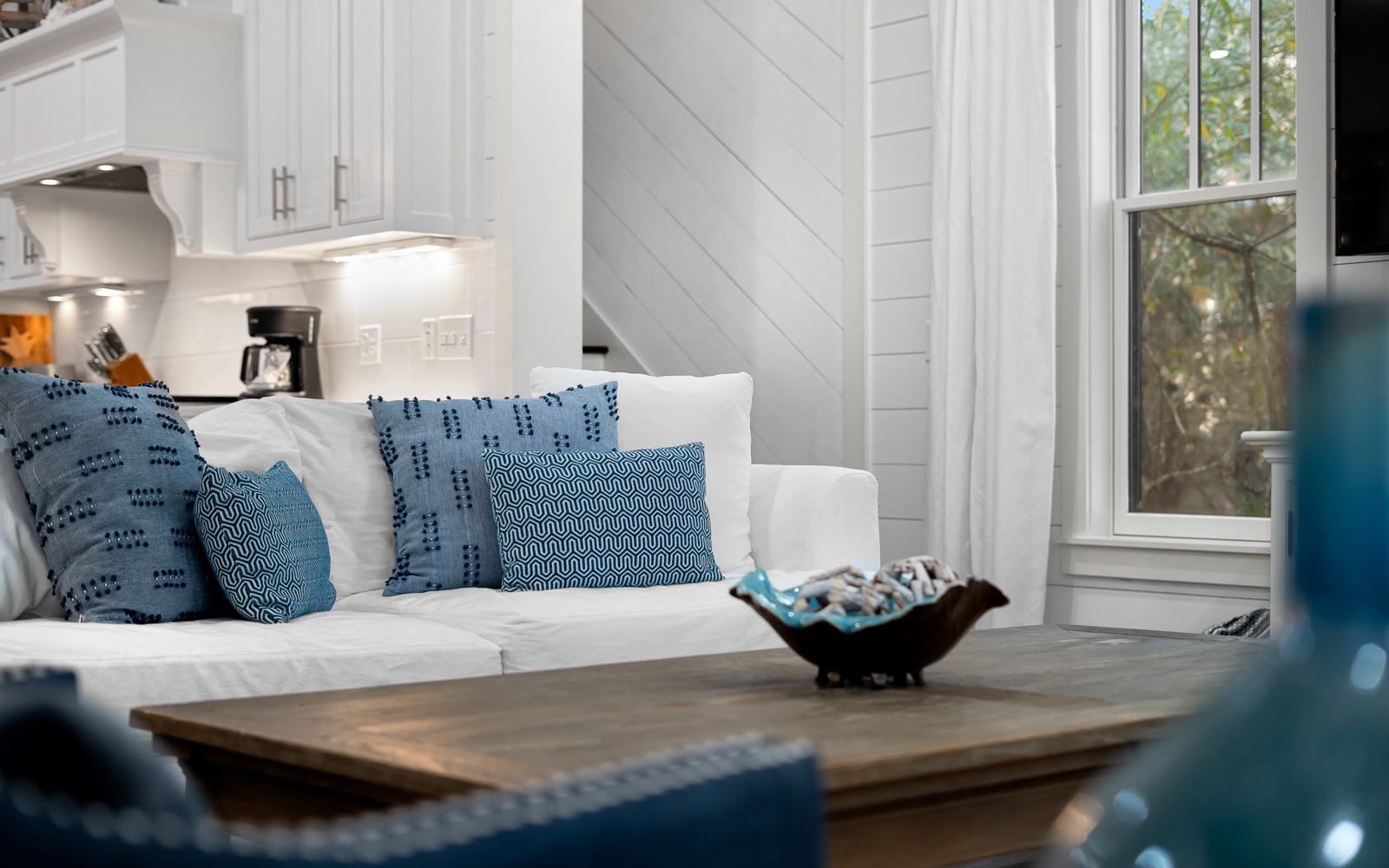 Sink into this cozy white sofa with plush blue pillows, where natural light streams through your windows as you unwind in style.