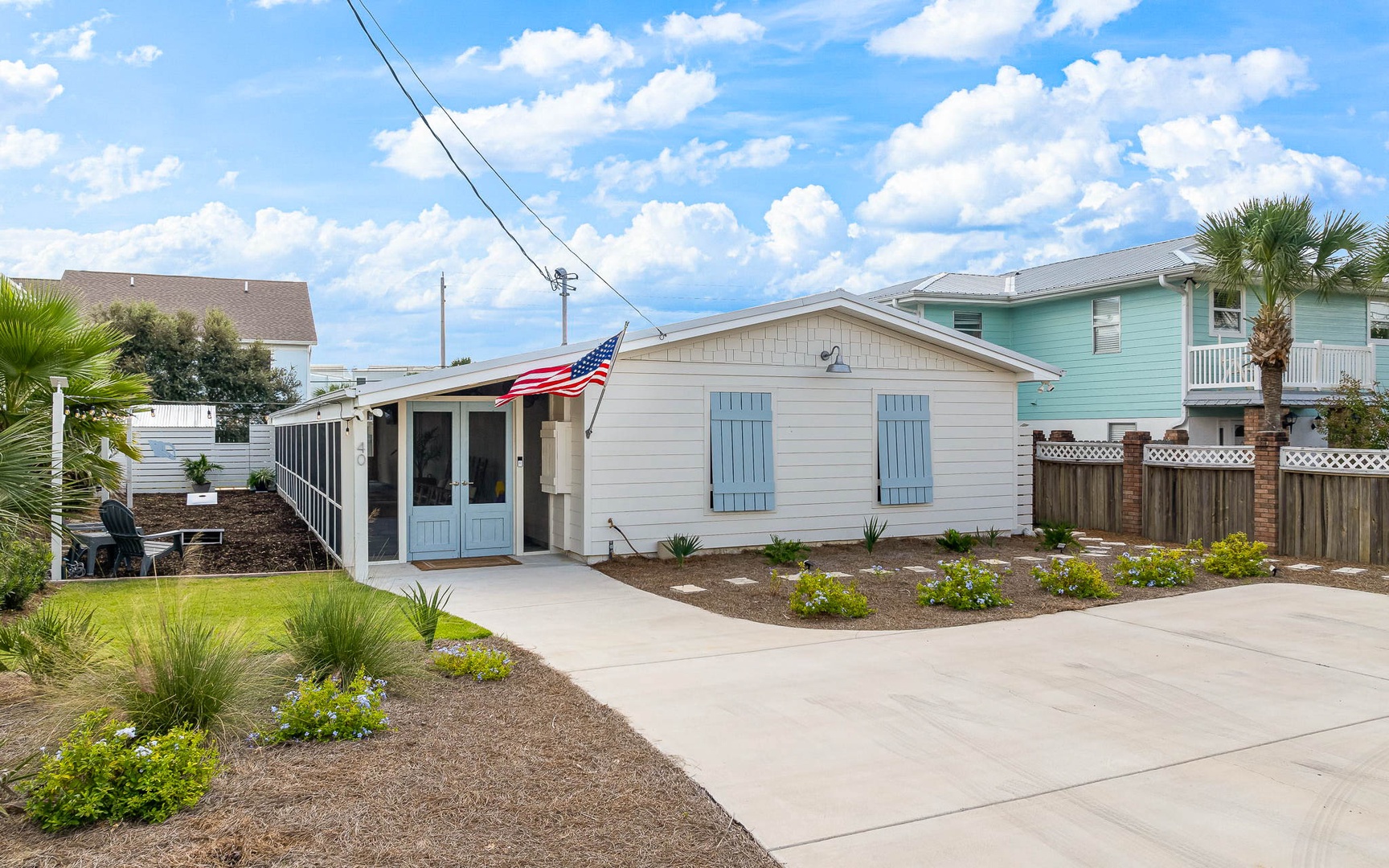 Charming coastal cottage with blue shutters and patriotic flair in a peaceful residential neighborhood.