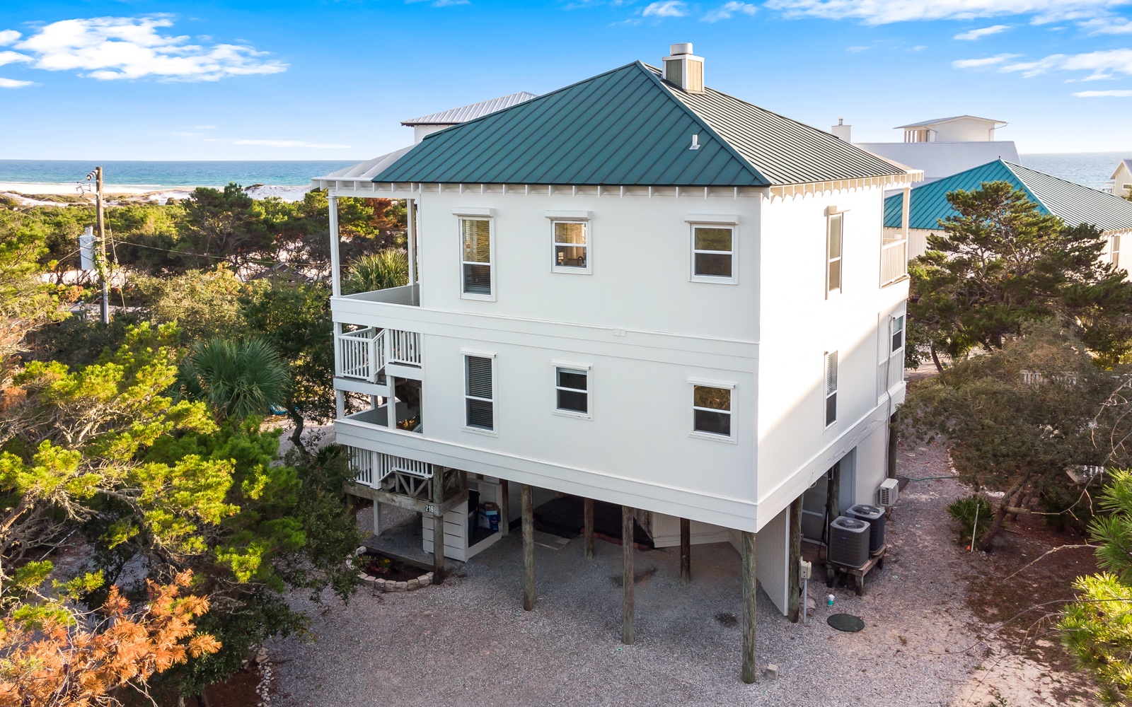 Elevated coastal home with distinctive green metal roof sits surrounded by natural vegetation just steps from the beach.