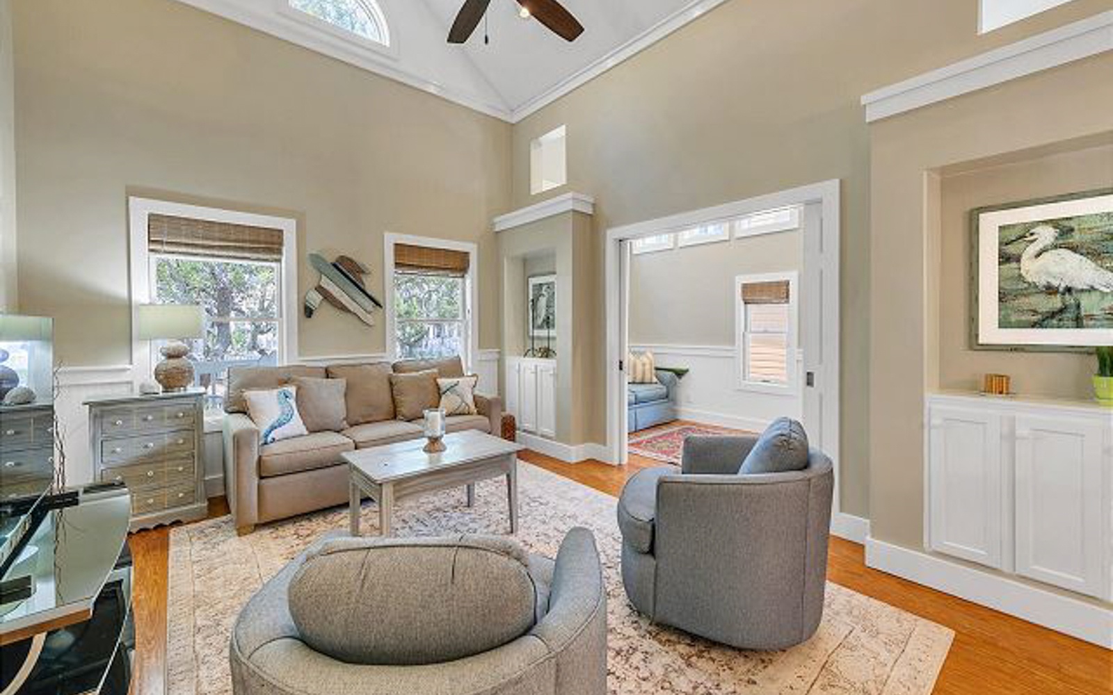 Relax in this elegant living room with vaulted ceilings, plush seating, and natural light streaming through bamboo shades.