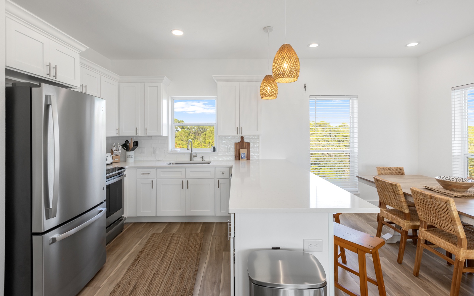 Your bright, modern kitchen awaits with sleek white cabinetry, stainless steel appliances, and warm woven pendant lights creating the perfect cooking retreat.