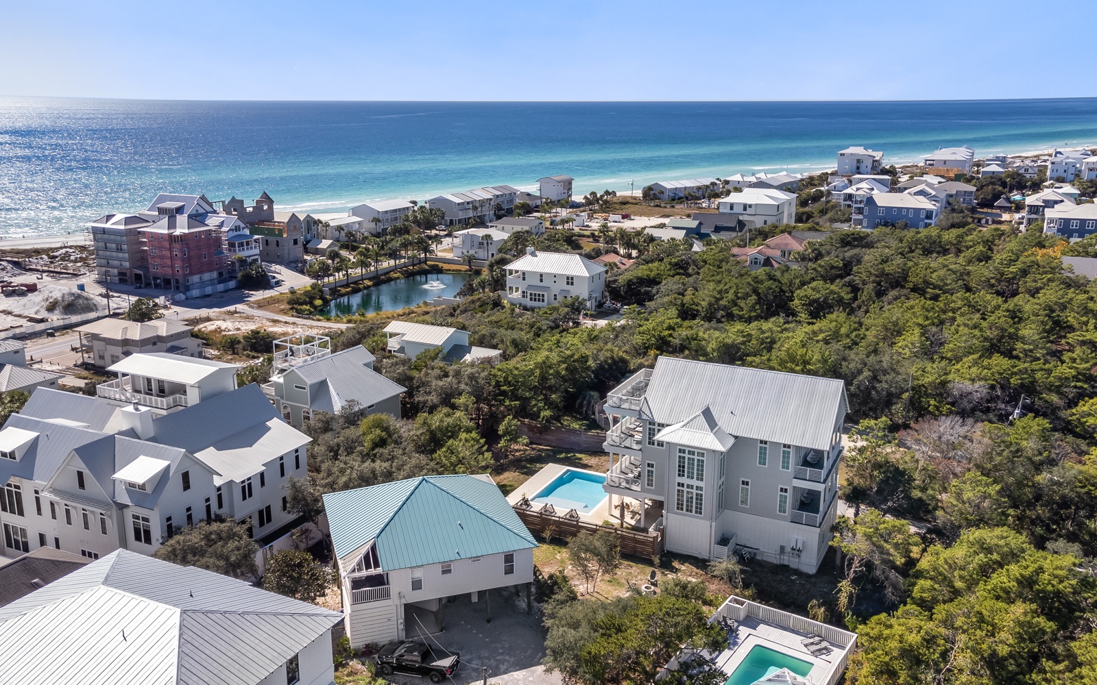 Aerial view of a coastal vacation rental community nestled among lush trees, just steps from pristine white sand beaches and turquoise waters.