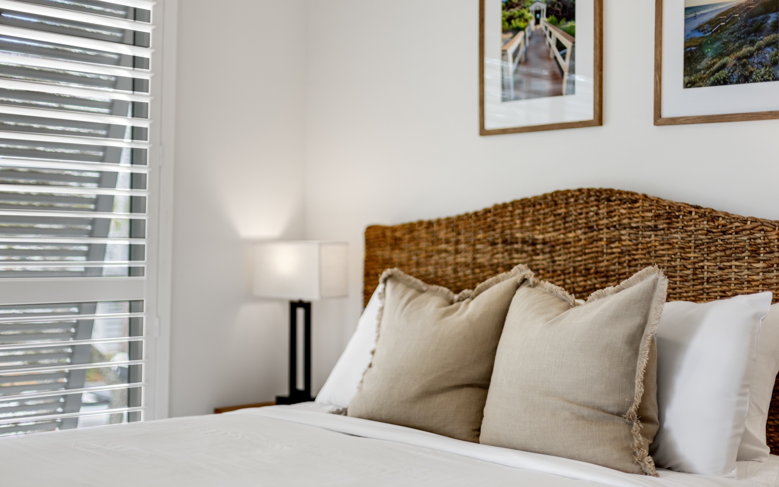 Sink into this beautifully appointed bed with its woven headboard and plush pillows, where natural light filters through blinds creating your perfect retreat.