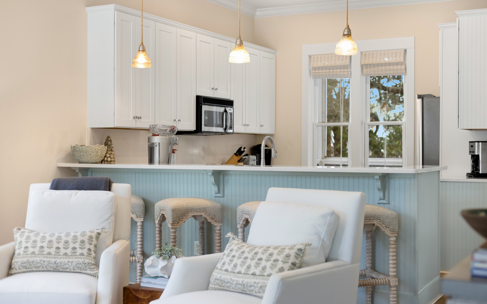 Relax in your bright coastal kitchen featuring white cabinetry, modern appliances, and charming pendant lighting perfect for morning coffee.