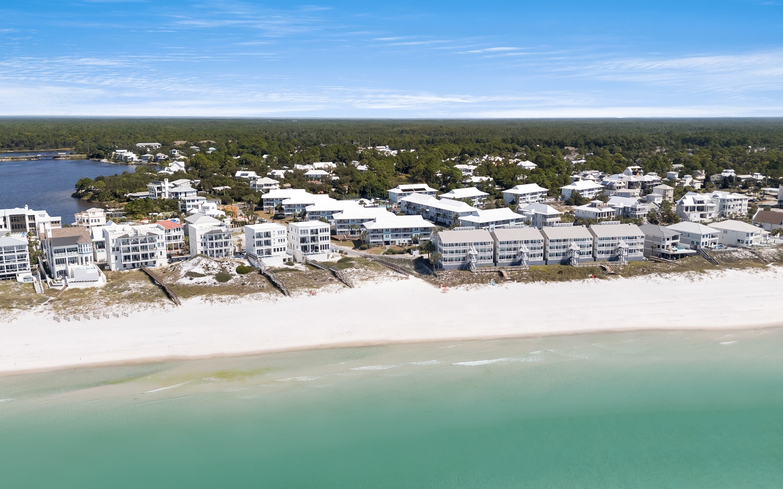 Aerial view of beachfront properties nestled along pristine white sand and emerald waters, surrounded by lush coastal forest.