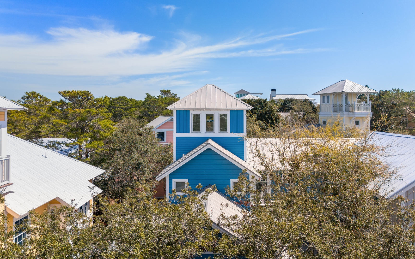 Charming coastal neighborhood featuring colorful beach houses nestled among mature trees under bright blue skies.