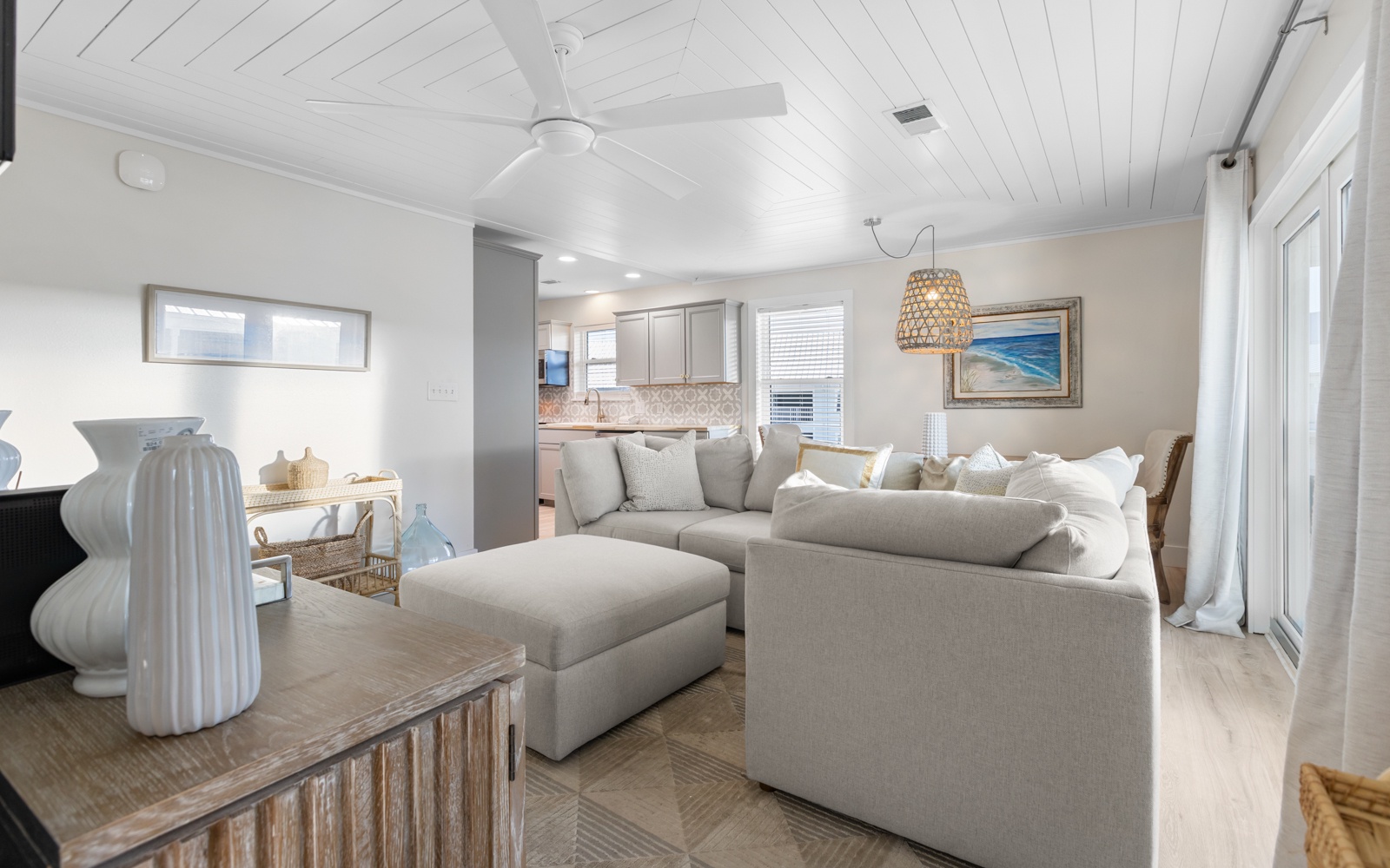 Relax in your airy coastal living room with plush sectional seating and modern kitchen beyond.