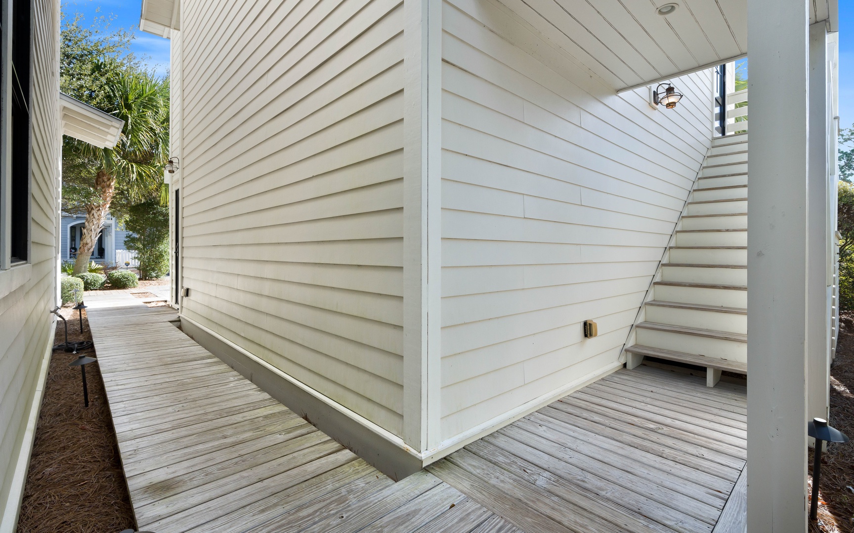 A covered outdoor area beneath the property, featuring white architectural elements and natural wood decking.