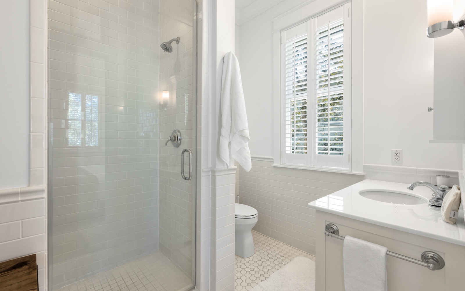 Step into your private spa-like bathroom with a luxurious glass shower, pristine white fixtures, and natural light streaming through plantation shutters.