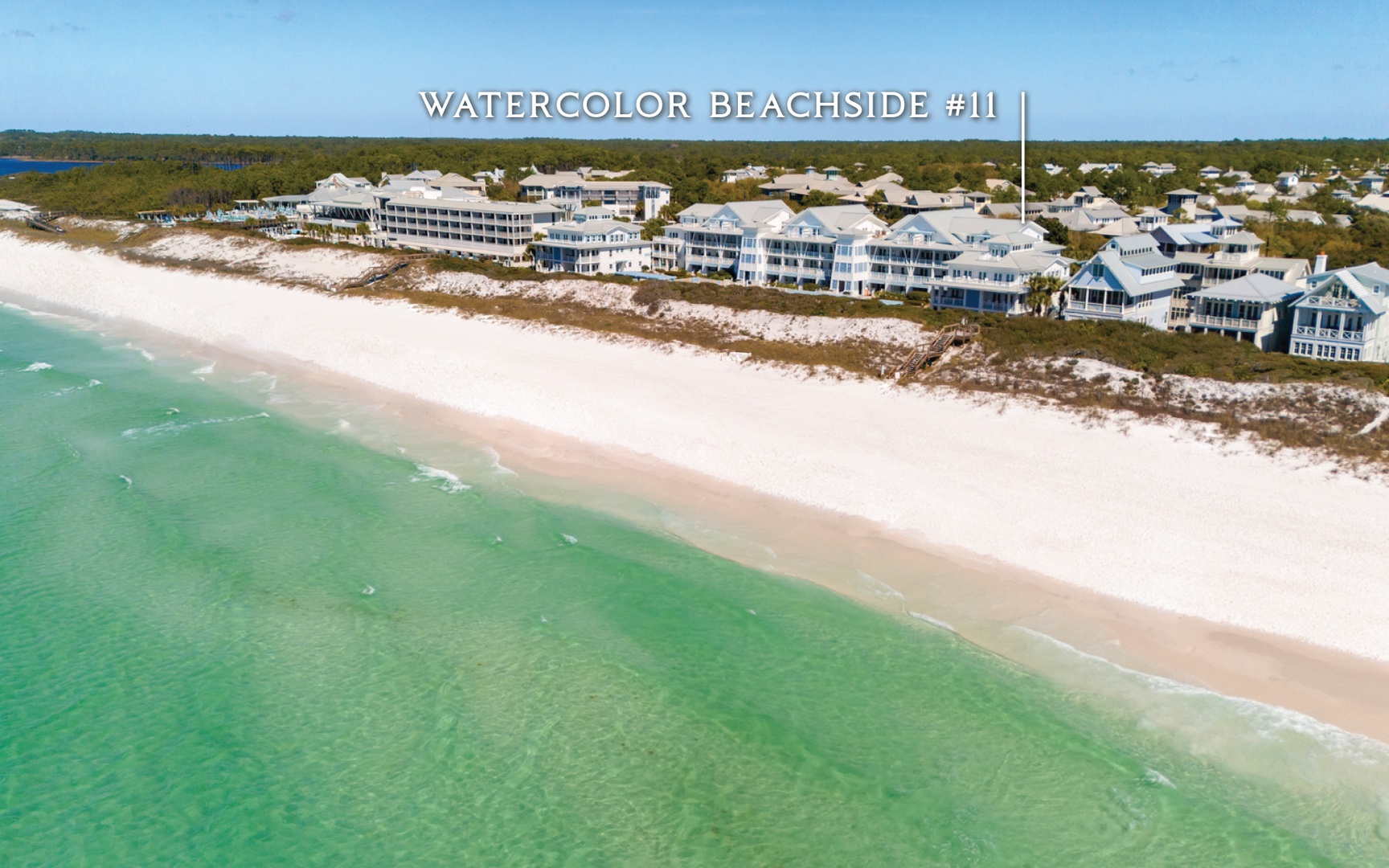Aerial view of beachfront properties along pristine white sand beach with turquoise waters and coastal community.