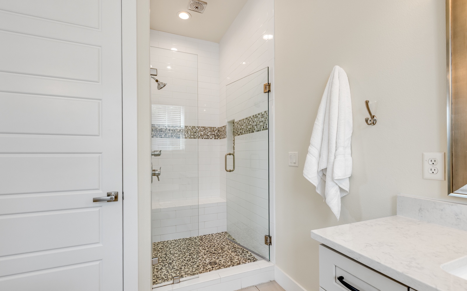 Step into your pristine bathroom featuring a spacious glass-enclosed shower with designer mosaic tile accents and fluffy towels awaiting your arrival.