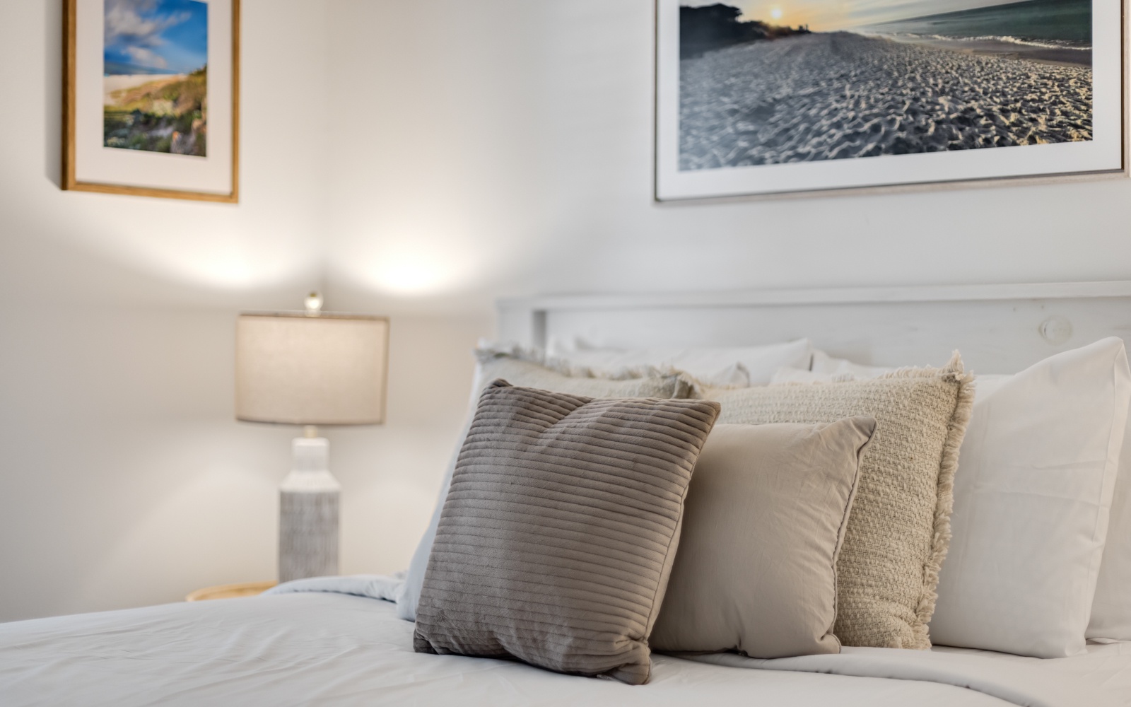 Sink into plush pillows and soft linens in your serene bedroom retreat, where coastal artwork and warm lighting create the perfect ambiance for restful nights.