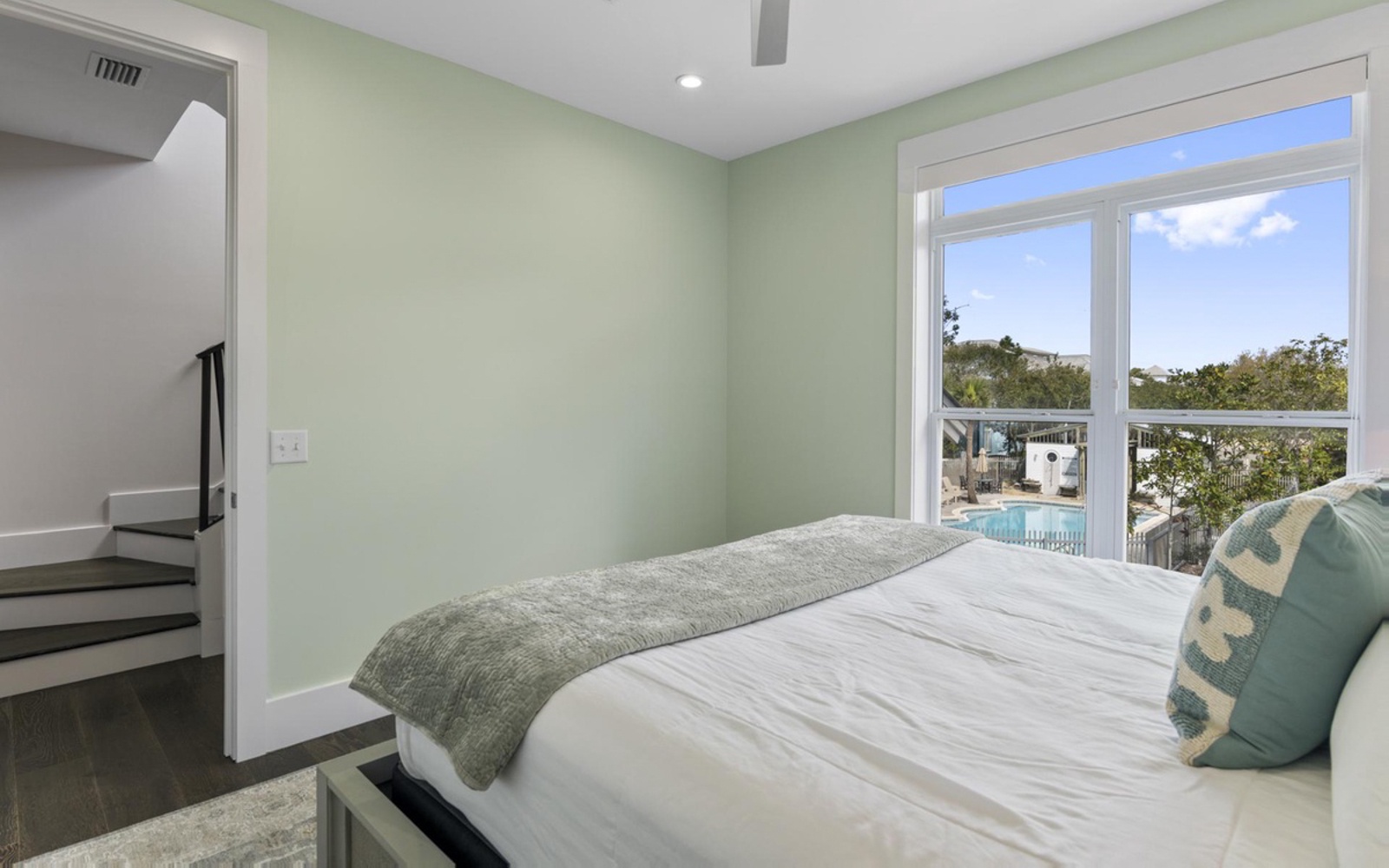 Drift off in this serene bedroom where soft green walls and crisp linens create your perfect retreat, with pool views beyond.