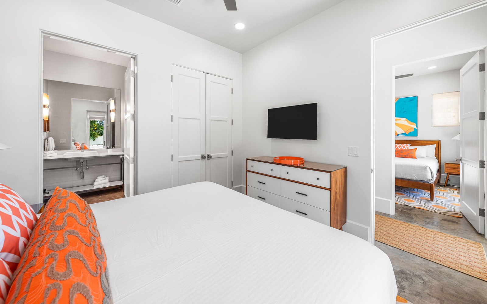Your bright bedroom features a comfortable bed, wall-mounted TV for movie nights, and modern furnishings with vibrant orange accents.
