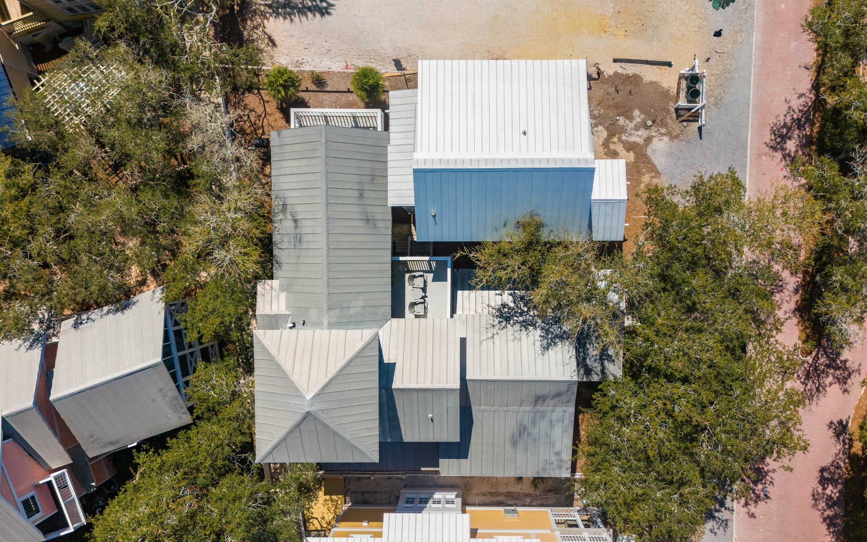 Aerial view of the modern property showcasing distinctive architecture with white metal roofing and blue accents nestled among mature trees.