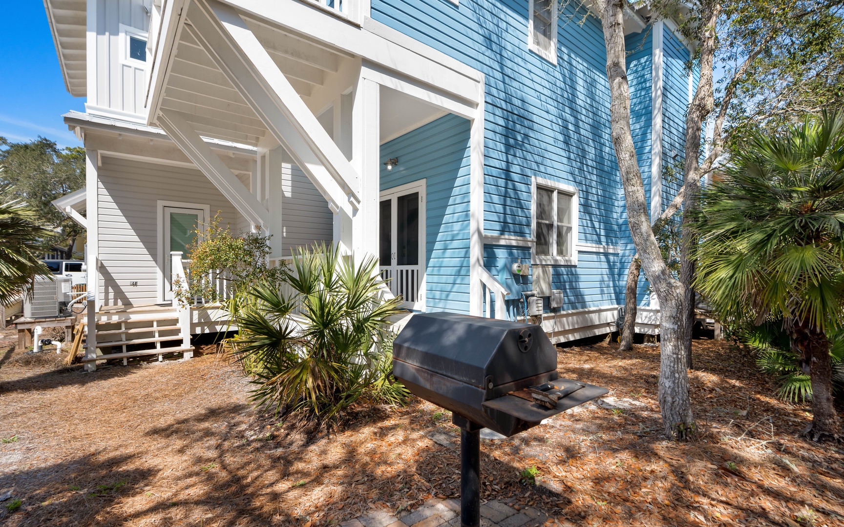 Charming coastal cottages with a dedicated BBQ grill for outdoor dining under palm trees and clear blue skies.