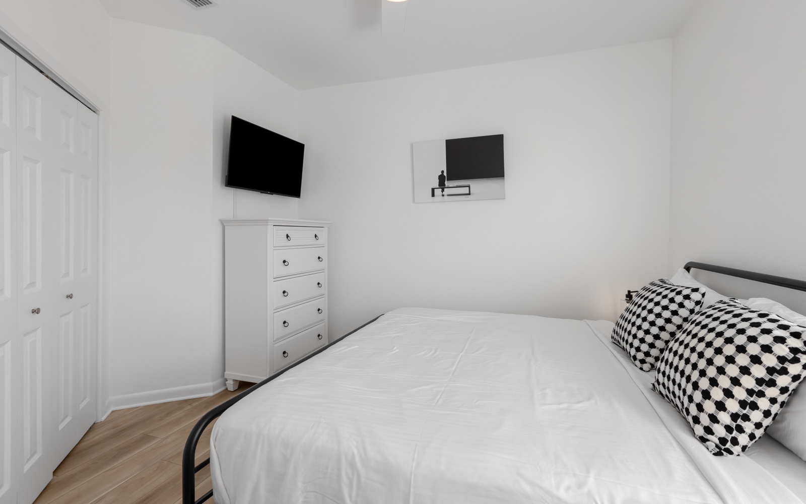 Unwind in your modern bedroom featuring crisp white linens, a wall-mounted TV, and stylish furnishings for peaceful nights.