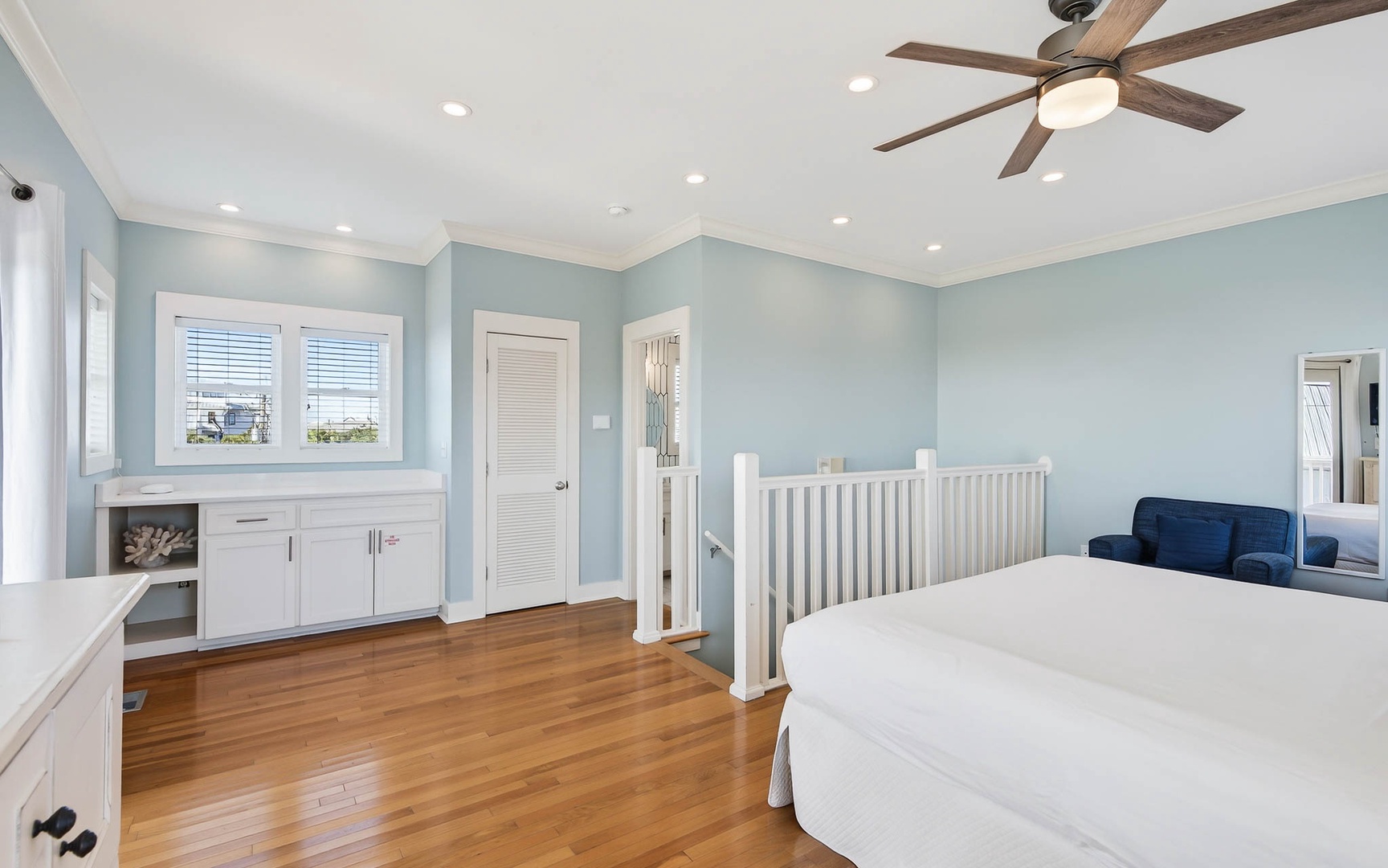 Unwind in your peaceful bedroom featuring warm hardwood floors, soothing blue walls, and a ceiling fan to keep you comfortable.