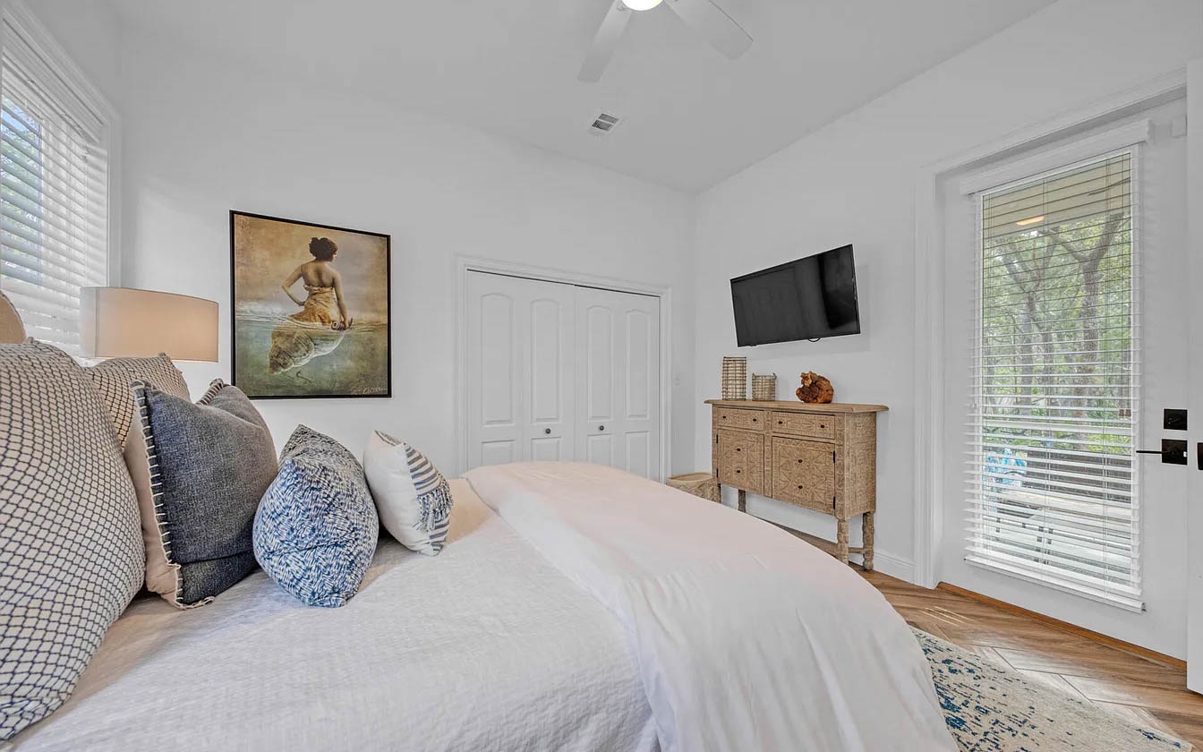 Sink into plush pillows and drift off in this serene bedroom, where natural light filters through blinds and charming artwork sets a peaceful tone.