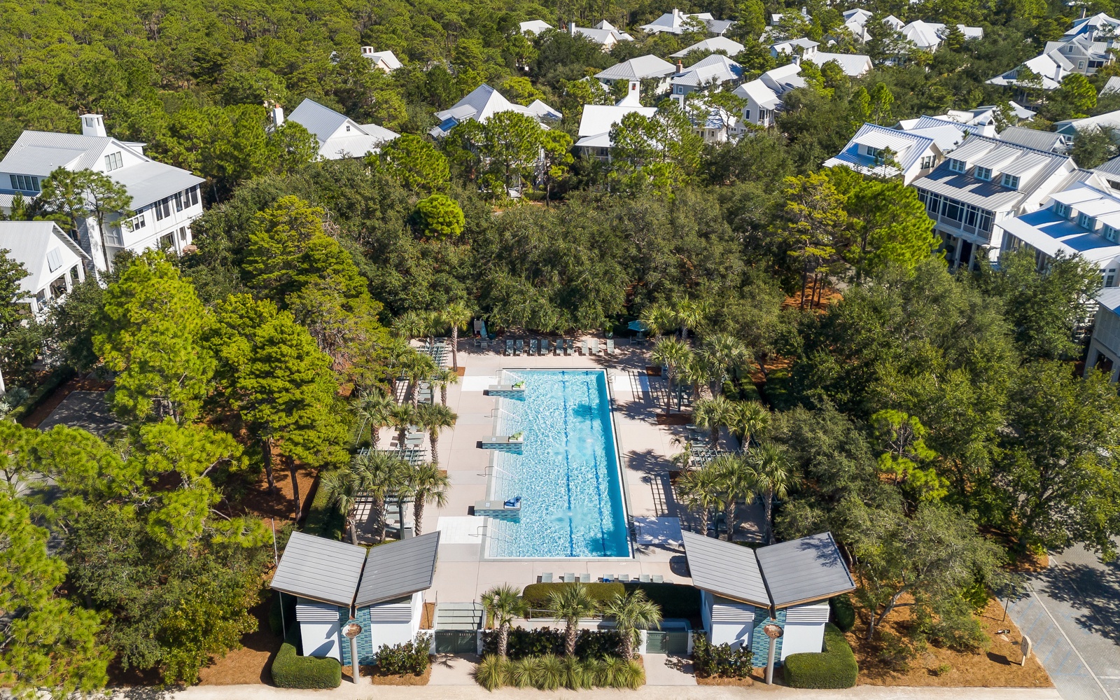 Aerial view of a pristine resort community featuring a sparkling pool surrounded by lush trees and elegant white homes.
