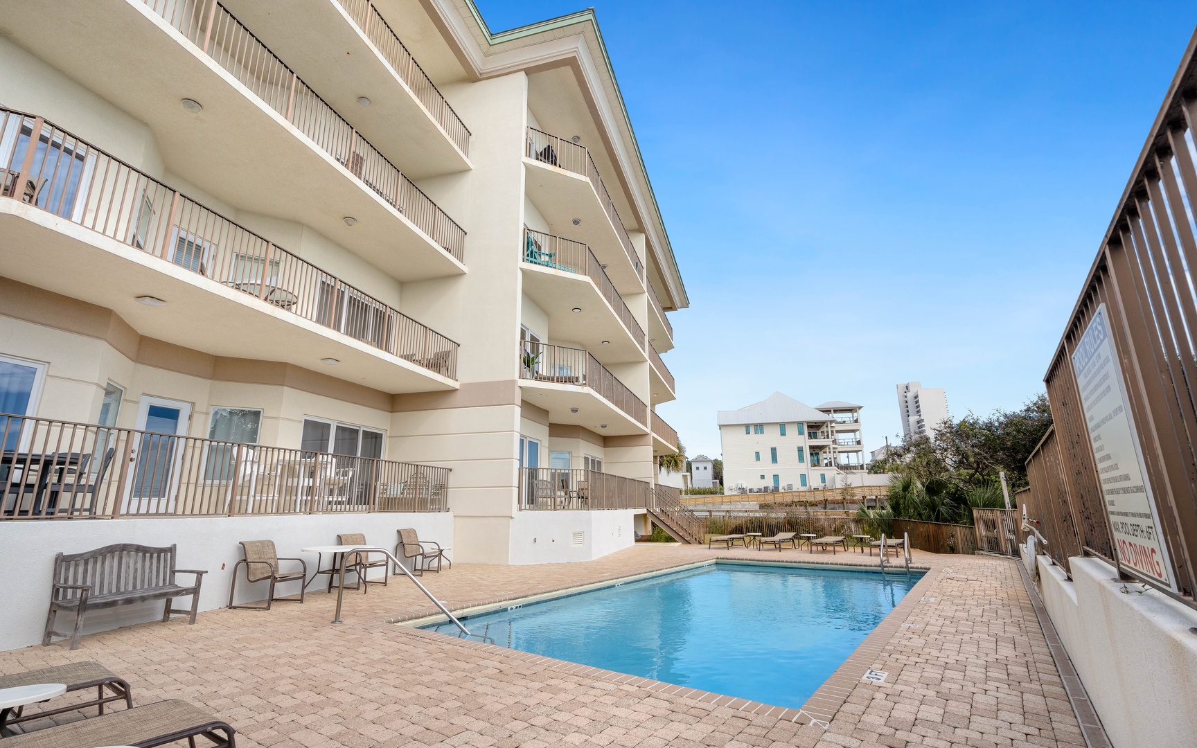 Modern beachside property featuring multiple floors of balconied accommodations surrounding a pristine swimming pool area with comfortable patio seating.