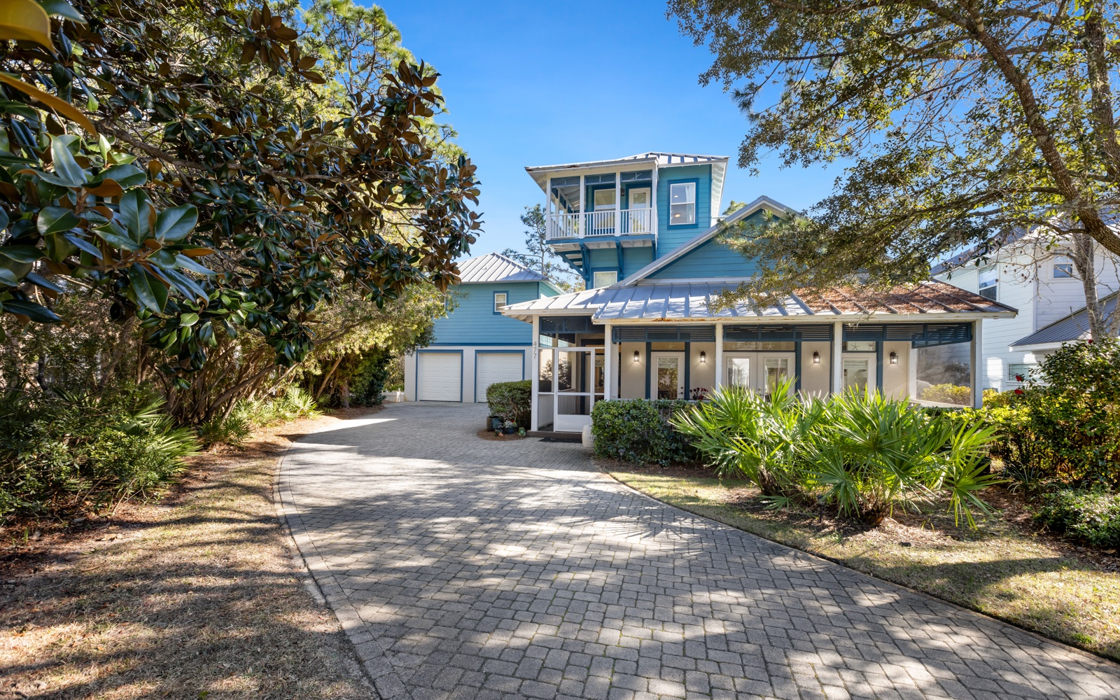 Charming coastal home with lush landscaping and brick-paved driveway creates a welcoming arrival experience in this peaceful neighborhood setting.