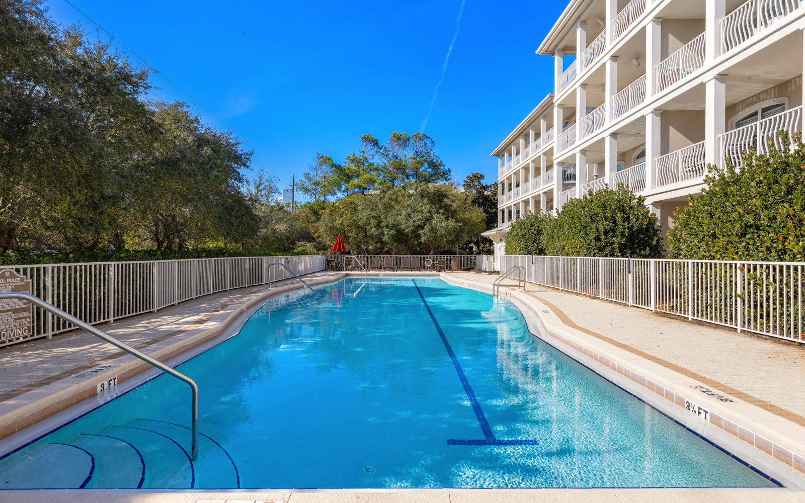 A crystal-clear pool awaits your perfect vacation day, surrounded by lush trees and bright blue skies.