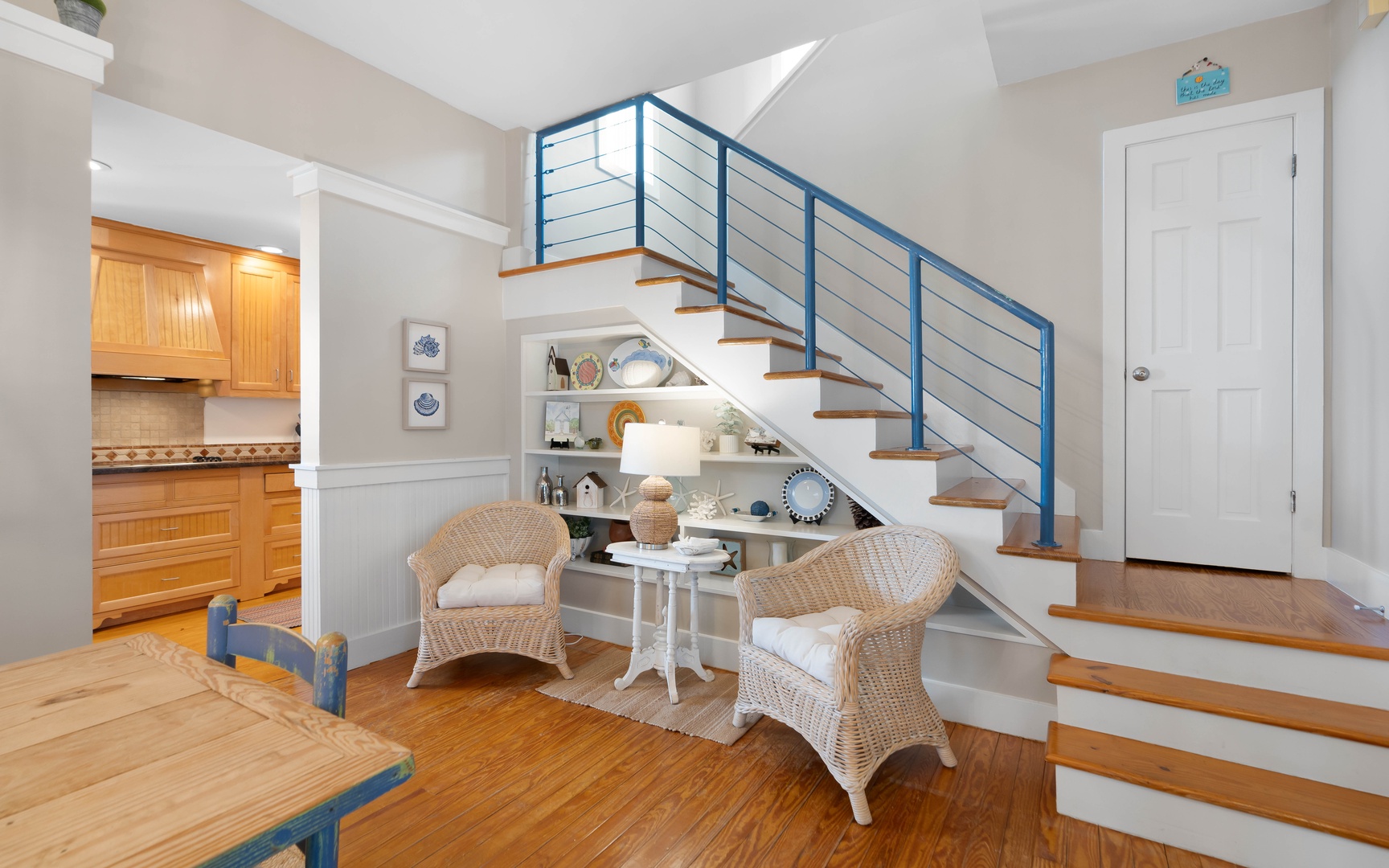 Your charming living space features nautical touches and cozy wicker seating beneath sleek stairs, perfect for morning coffee or evening relaxation.