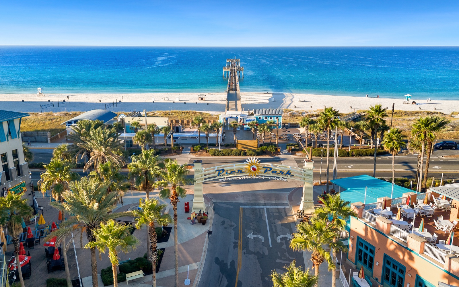 Aerial view of Pier Park entertainment complex with pristine beach access, palm-lined streets, and sparkling blue Gulf waters nearby.