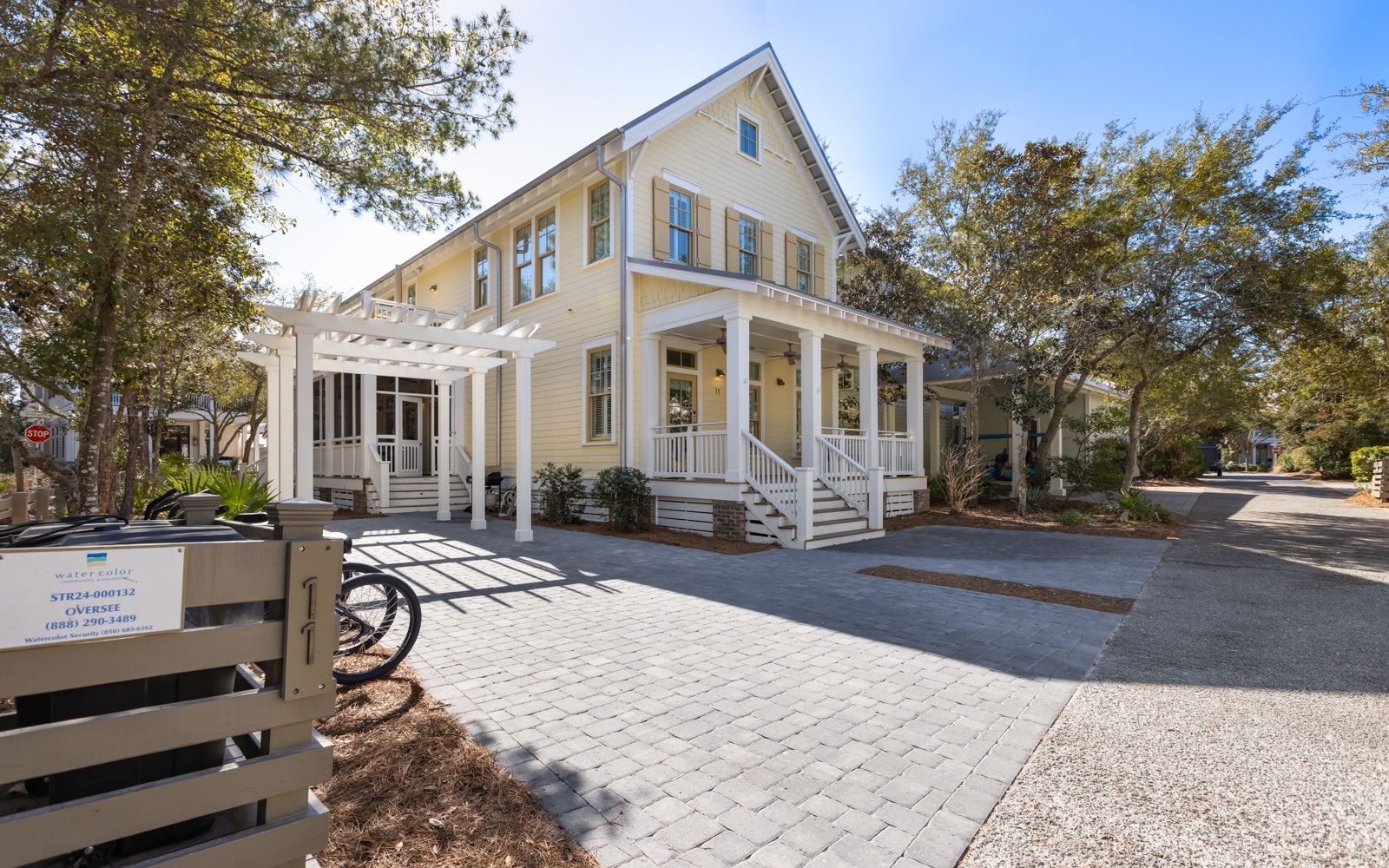 Charming coastal-style cottage with wraparound porch and mature trees creates a welcoming retreat in a peaceful neighborhood setting.
