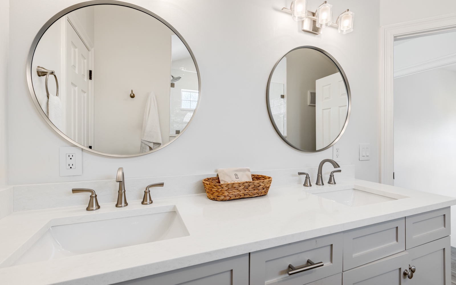 Your pristine master bathroom features dual vanities with elegant round mirrors and soft pendant lighting for your morning routine.