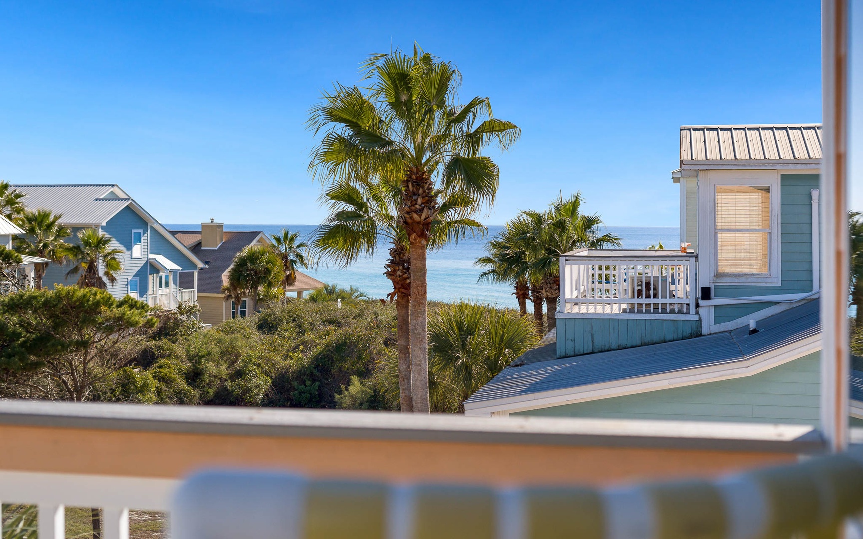 Coastal neighborhood with colorful beach houses and swaying palm trees beneath clear blue skies near the ocean.