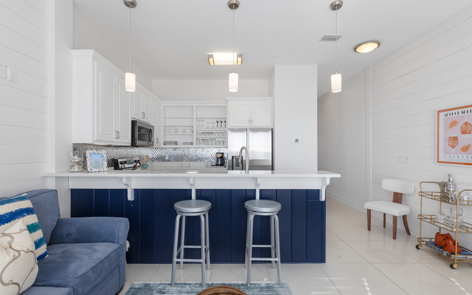 Your sleek kitchen features navy blue island seating, modern pendant lighting, and stainless steel appliances for effortless meal prep.