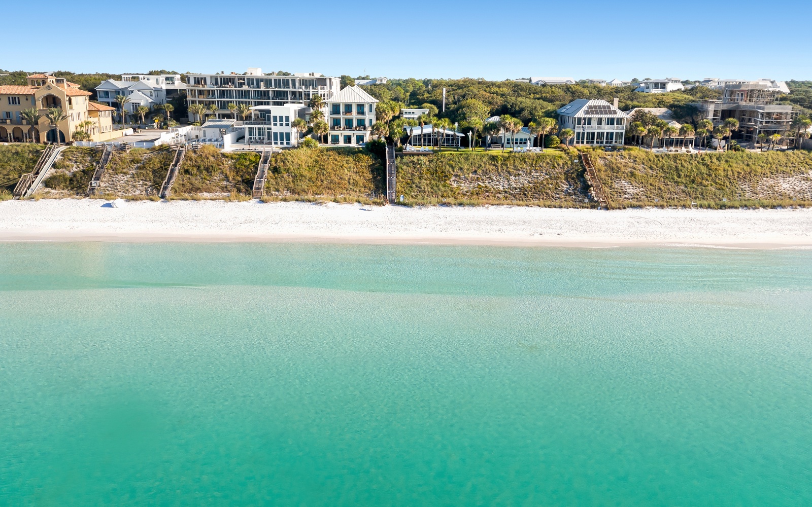 Stunning beachfront properties line pristine white sand shores with crystal-clear turquoise waters and lush coastal vegetation.