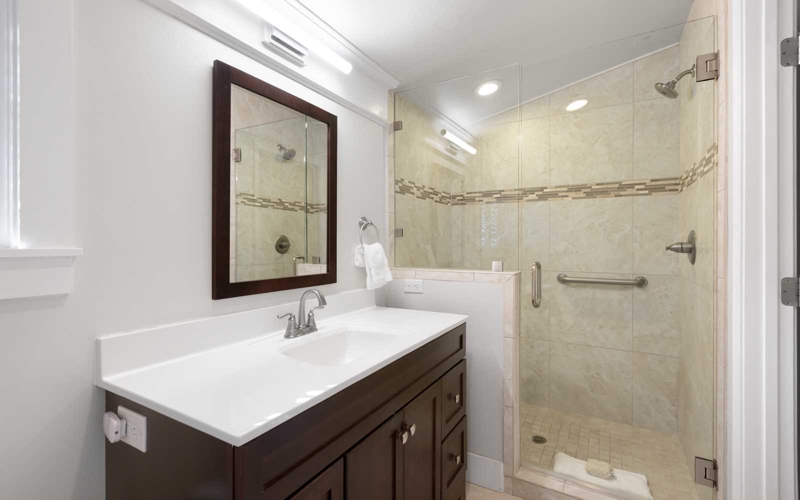 Your private bathroom features elegant white countertops, warm wood cabinetry, and a spacious glass-enclosed shower with beautiful tile details.