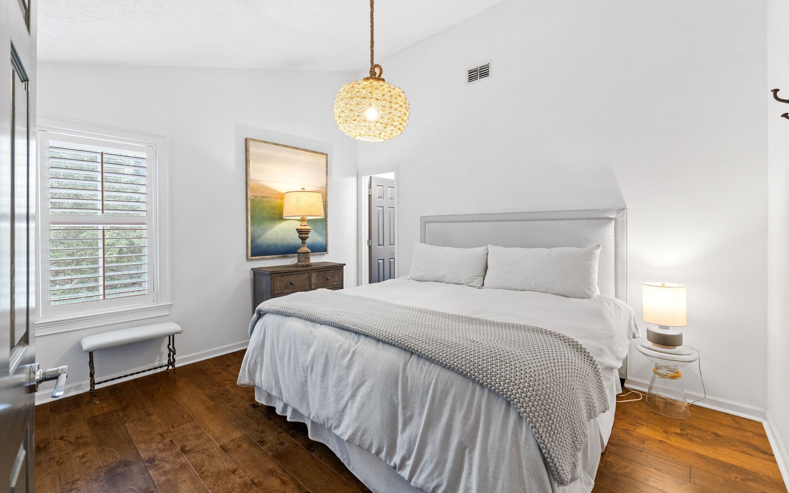 Sink into crisp linens and soft textures in your peaceful bedroom sanctuary, where warm lighting and coastal artwork create the perfect retreat.