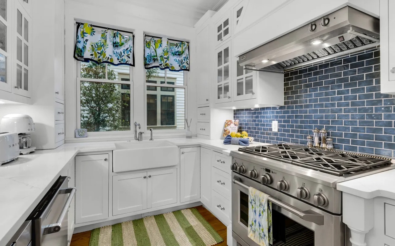 Your bright, airy kitchen features pristine white cabinetry, professional-grade stainless steel appliances, and a stunning blue subway tile backsplash that catches the natural light.