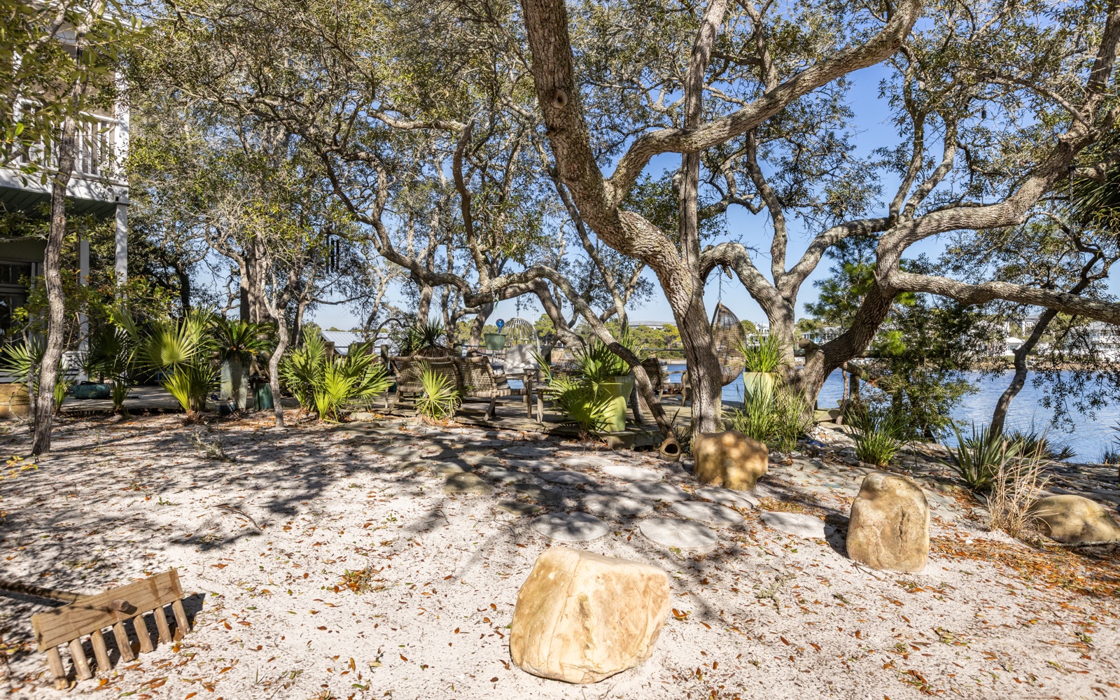 Waterfront retreat with majestic oak trees creating natural shade over sandy grounds and tropical landscaping near the shoreline.