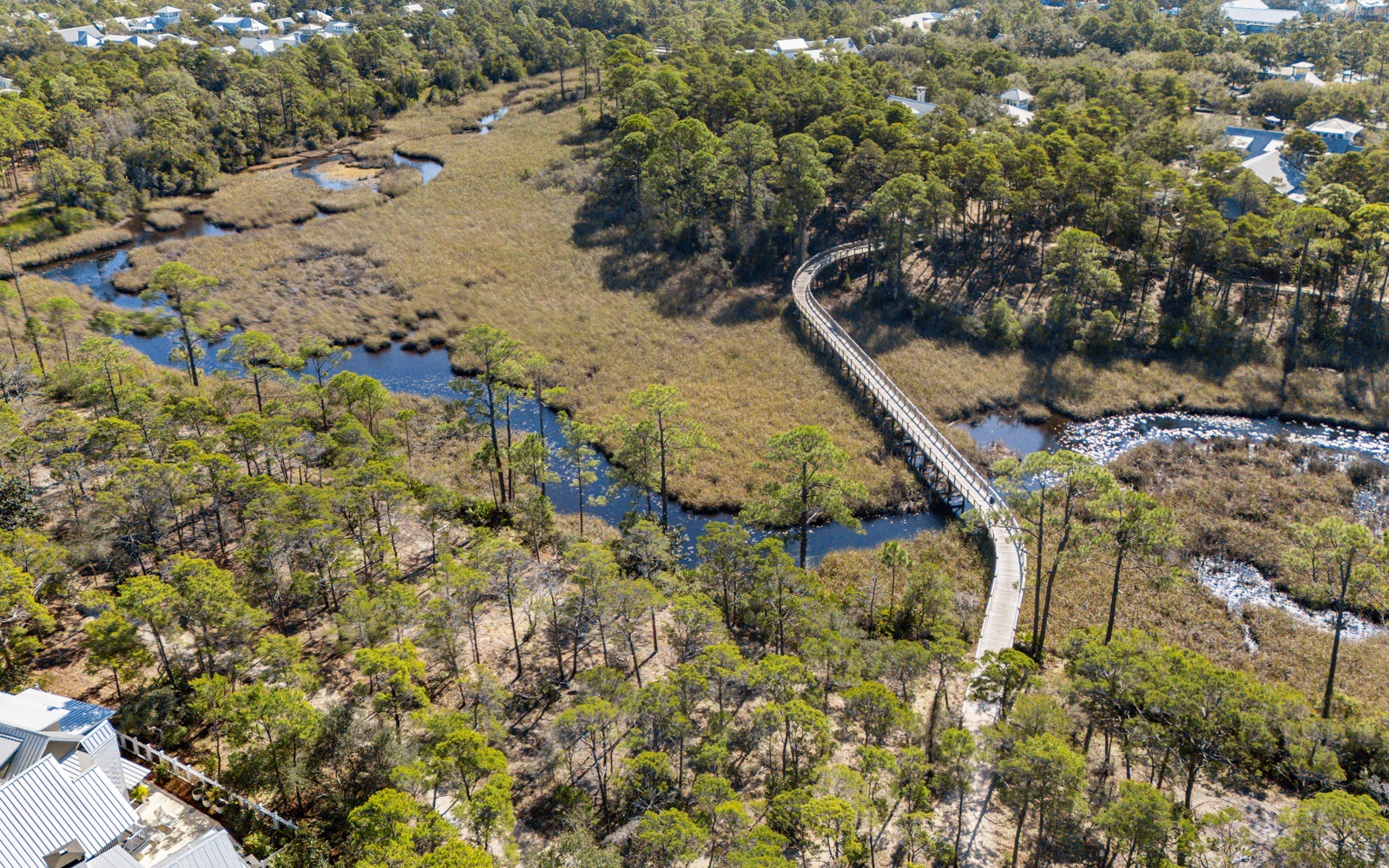 Aerial view reveals a scenic boardwalk winding through coastal wetlands and forest, connecting the residential neighborhood to natural preserves.