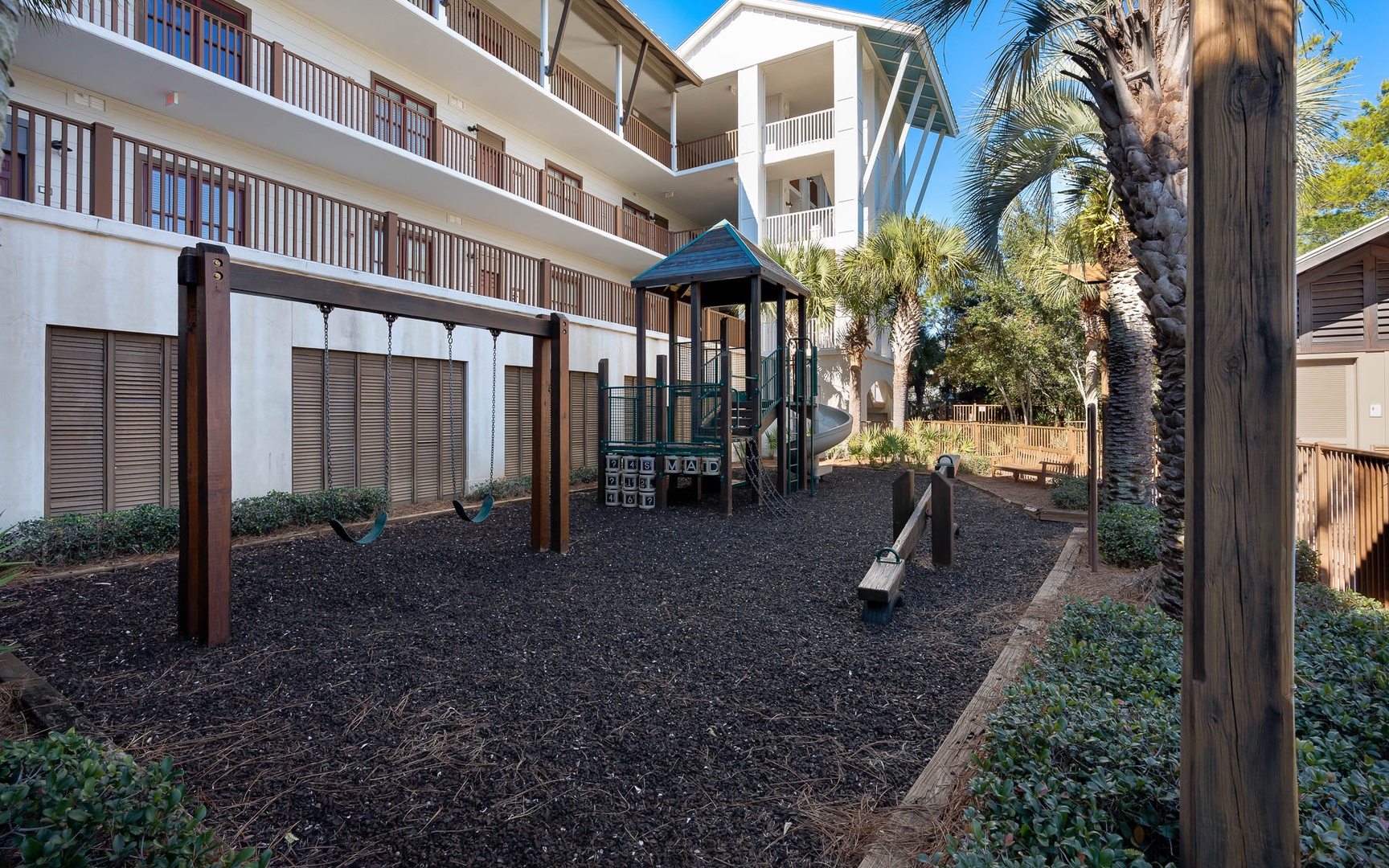 Safe playground area with swings and climbing structure surrounded by tropical palms and resort buildings.