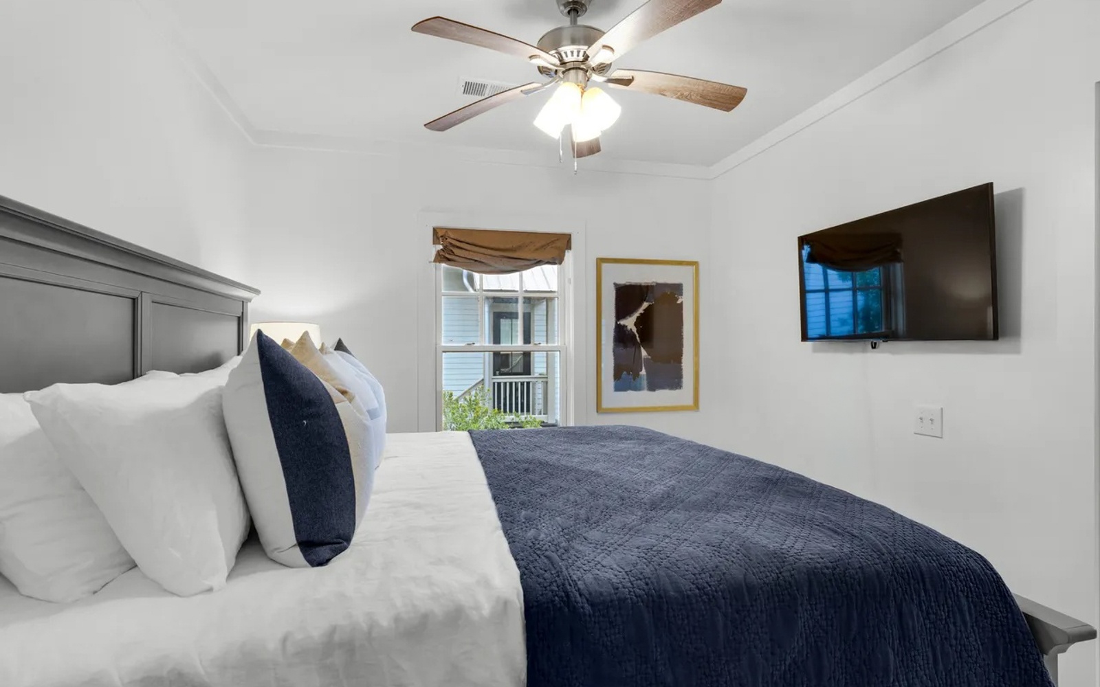 Your cozy bedroom features crisp white linens with navy accents, a ceiling fan for comfort, and a wall-mounted TV for relaxing evenings.