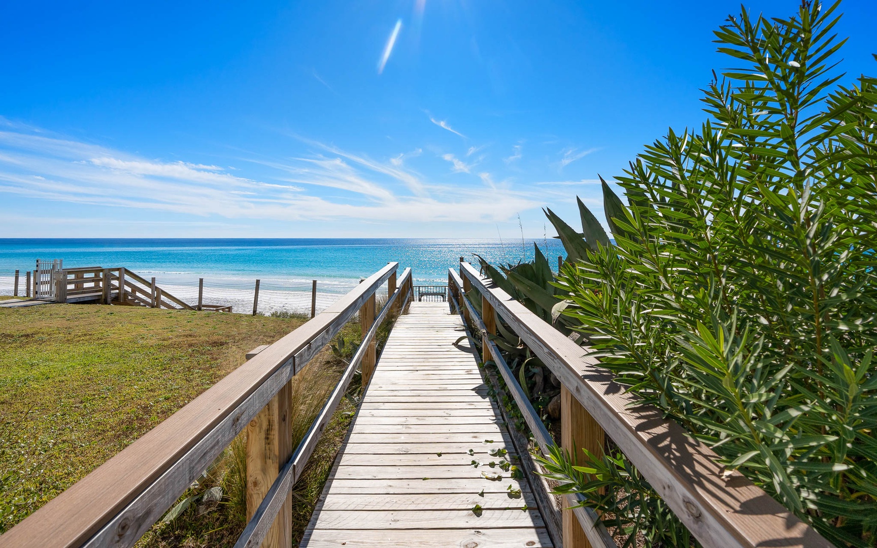 Wooden boardwalk leads directly to pristine turquoise waters and white sand beach under brilliant blue skies.