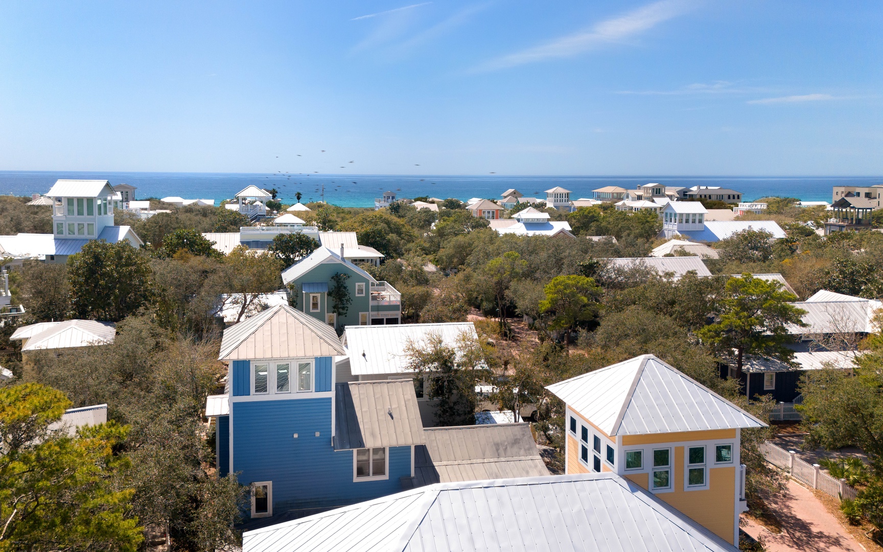 Coastal community with colorful beach houses nestled among mature trees, offering stunning ocean views and peaceful seaside living.