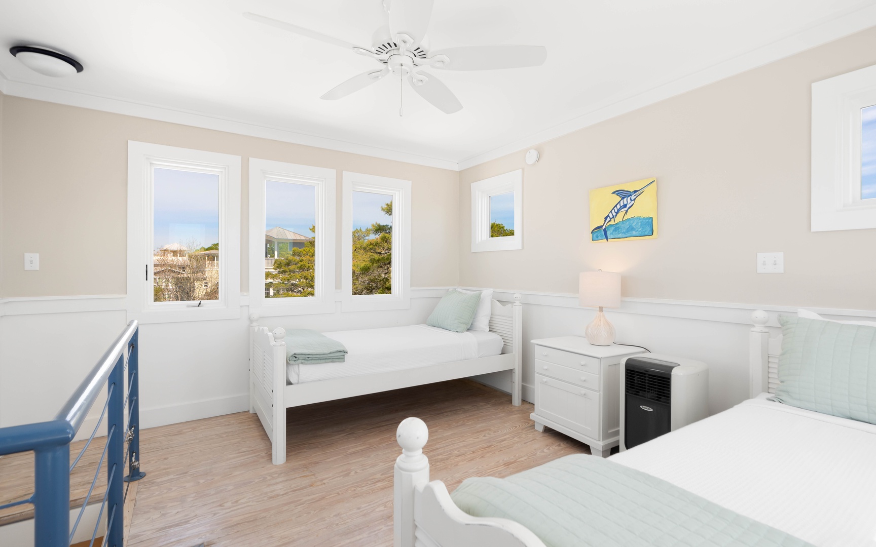 Your peaceful bedroom features twin beds with soft linens, ocean views through bright windows, and a gentle ceiling fan for comfort.