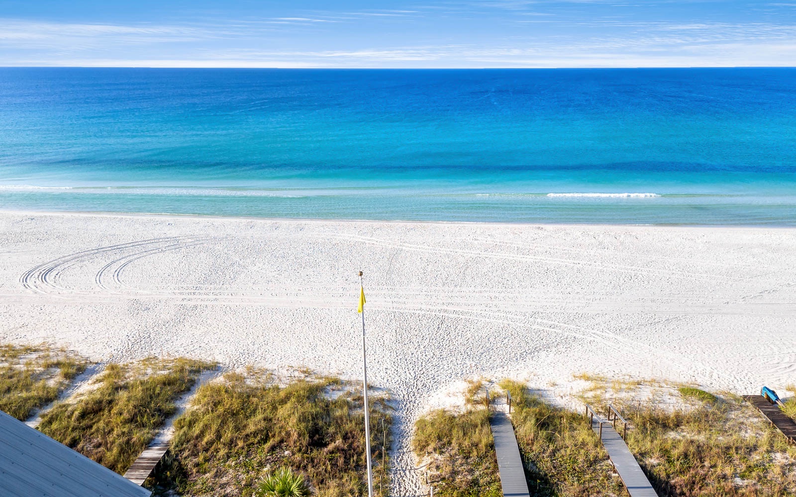 Pristine white sand beach stretches endlessly along crystal-clear turquoise waters, with wooden boardwalk leading to the shoreline.