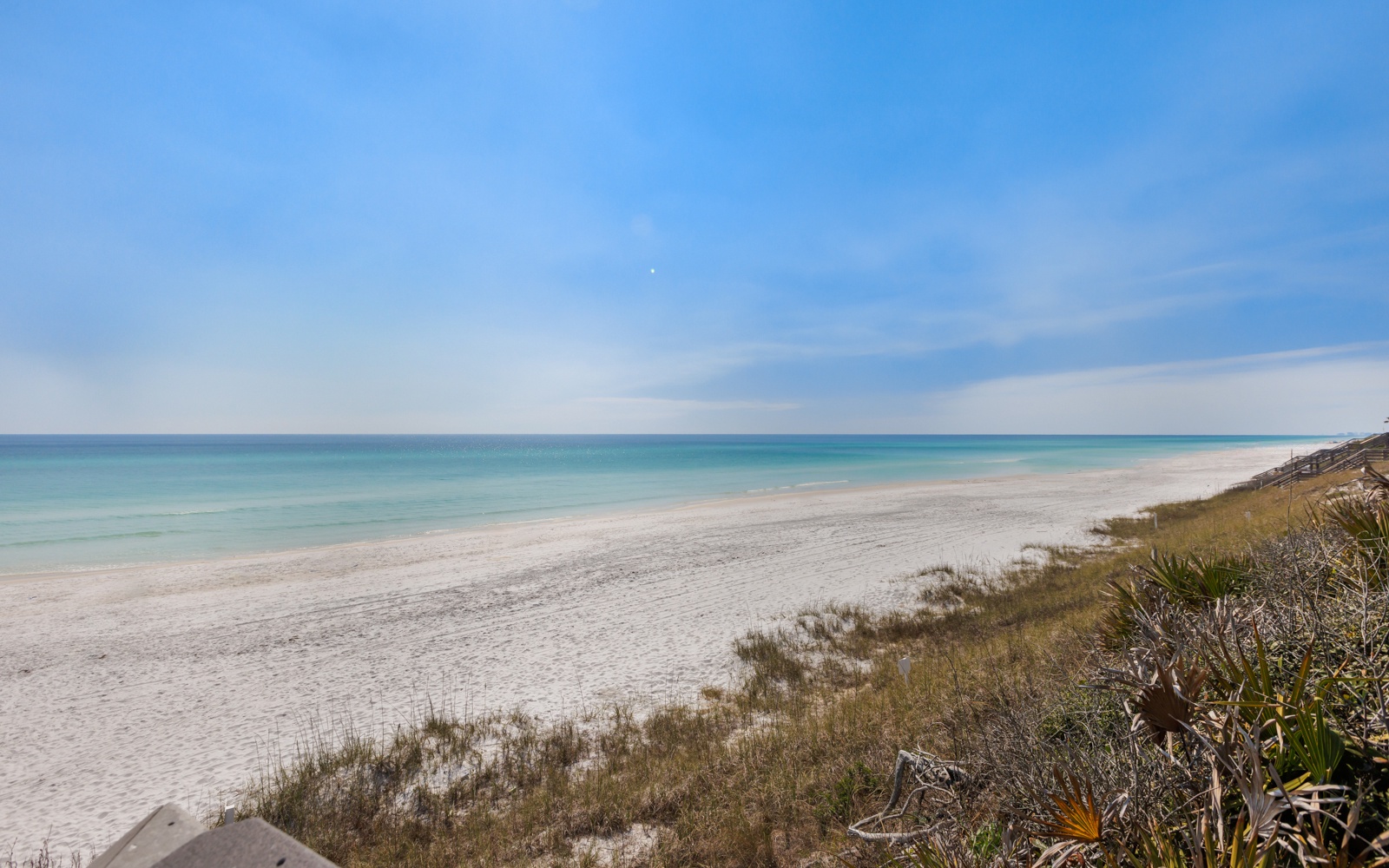 Pristine white sand beach stretches endlessly under brilliant blue skies, offering peaceful coastal retreat near the property.