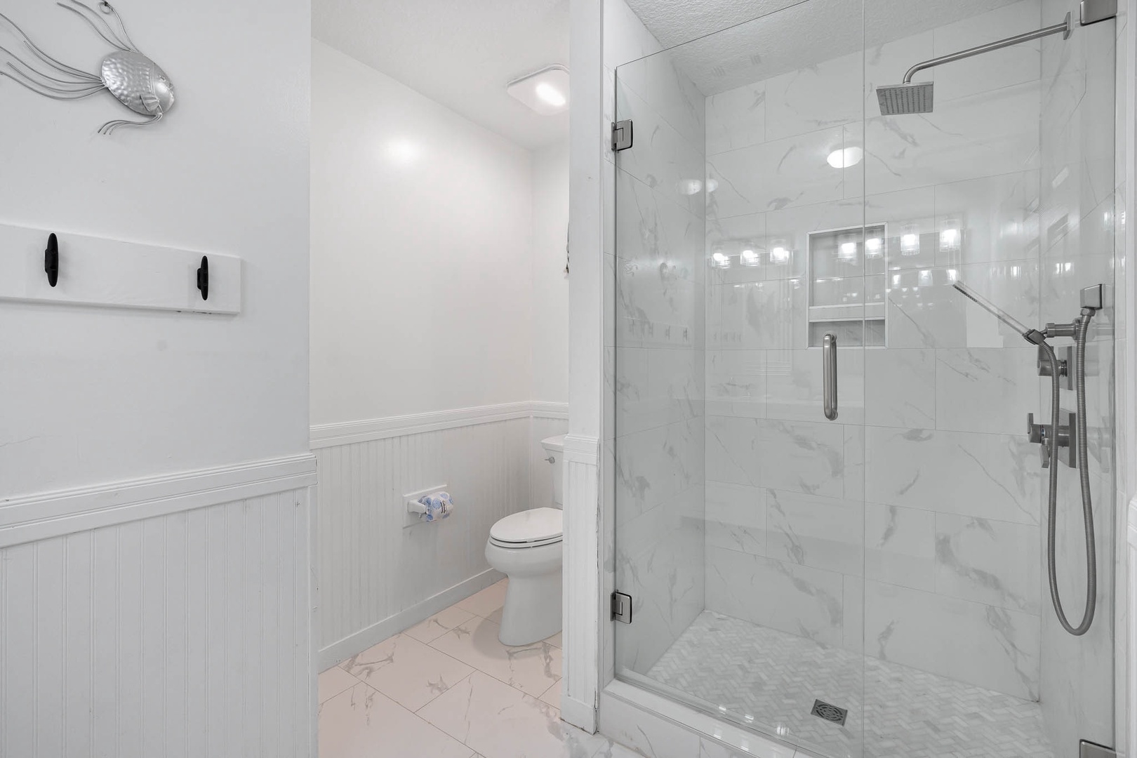 Step into your pristine marble bathroom where elegant white wainscoting meets a luxurious glass-enclosed shower with rainfall showerhead.