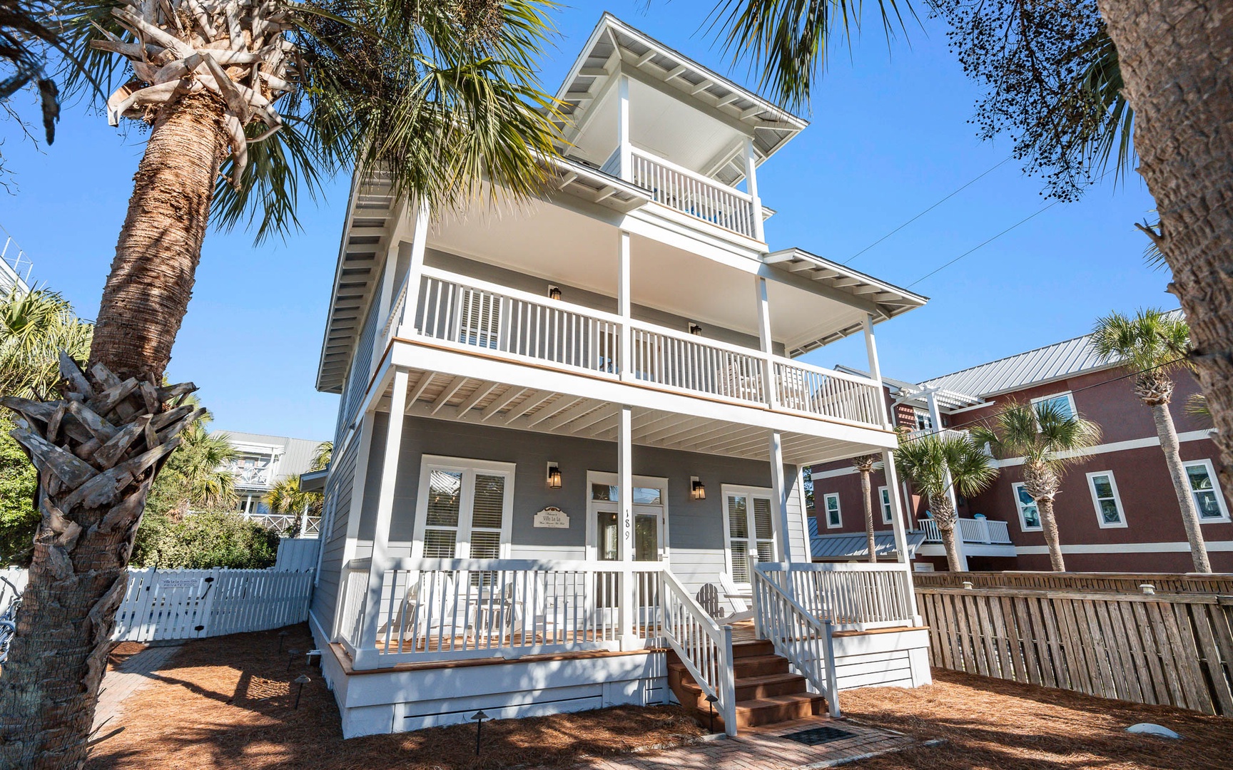 Multi-story coastal cottage with palm trees and bright blue skies frames this charming property entrance.